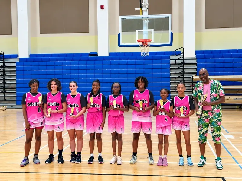 Girls youth basketball team in pink jerseys holding trophies with their coach | Cory McGee